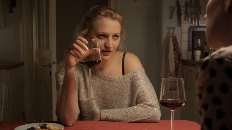 Kvinna sitter vid ett bord och håller ett klas vin, klipp från Exfrun